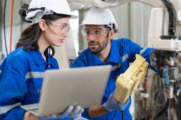 Male and female engineer training using remote controller control robot arm welding machine in...