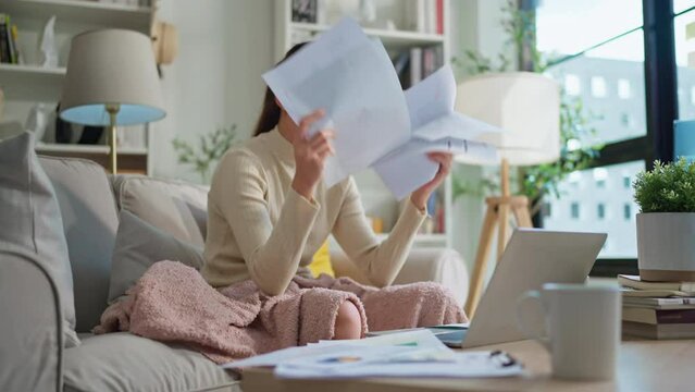 Woman going through bills, looking worried. Young adult asian woman female reading her bill papers and getting headache from stress Young asian woman at home paying online bills