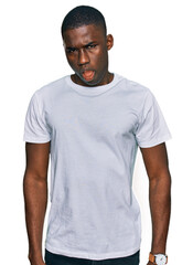 Young african american man wearing casual white t shirt in shock face, looking skeptical and sarcastic, surprised with open mouth