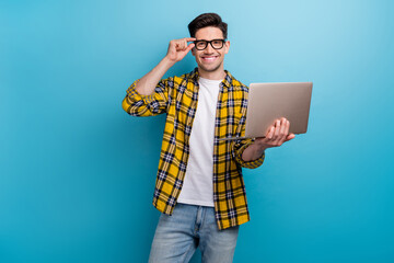 Portrait of clever cheerful guy with stubble wear checkered shirt touching glasses holding laptop isolated on blue color background - obrazy, fototapety, plakaty