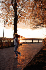 A little beautiful girl runs happily in torn jeans with long flowing hair against the background of a golden sunset.