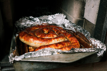 Homemade spiral sausage fried in a wood-burning stove. Meat cooking in a brick oven.
