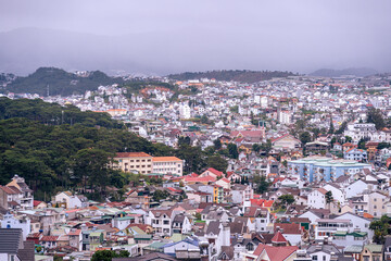 Fototapeta premium View on roofs in the city of Dalat. Da Lat and the surrounding area is a popular tourist destination of Asia. City with fogs and mountains
