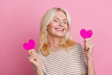 Photo of lovely cheerful person toothy smile closed eyes arms hold little heart symbol cards isolated on pink color background
