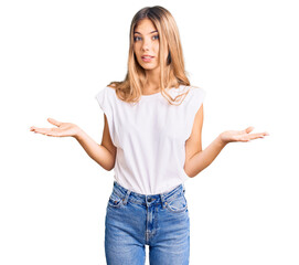 Beautiful caucasian woman with blonde hair wearing casual white tshirt clueless and confused expression with arms and hands raised. doubt concept.