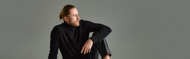 banner of bearded man in turtleneck sweater and black leather pants sitting on grey background