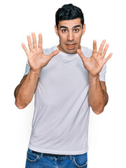 Naklejka premium Handsome hispanic man wearing casual white t shirt afraid and terrified with fear expression stop gesture with hands, shouting in shock. panic concept.