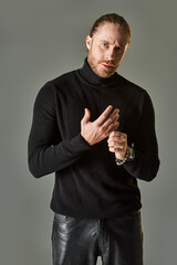 handsome bearded man in black turtleneck sweater wearing silver ring on finger on grey background