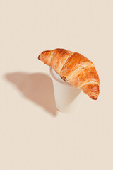 Fresh delicious croissants with an eco cup on a light background.