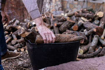 Hands of a man picking up firewood from the ground and putting it in a basket to move it.