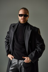 portrait of handsome male model in trendy sunglasses and black attire standing with hands in pockets