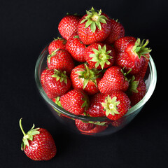 juicy red strawberries in a transparent glass bowl close-up, dark background, no people, minimalism