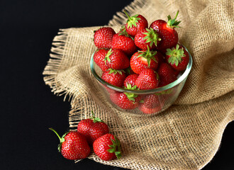 juicy red strawberries in a transparent glass bowl close-up, dark background, no people, minimalism