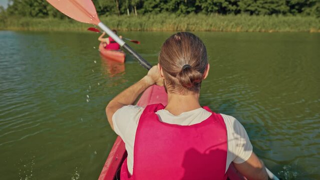 Rear view of man swimming behind woman in kayak. Resting on lake on sunny day. People in vests kayaking together. Recreation. River trip. Beautiful landscape. Concept of tourism.