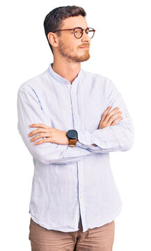Handsome young man with bear wearing elegant business shirt and glasses looking to the side with arms crossed convinced and confident
