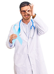 Handsome young man with bear wearing doctor uniform and holding blue ribbon smiling happy doing ok sign with hand on eye looking through fingers