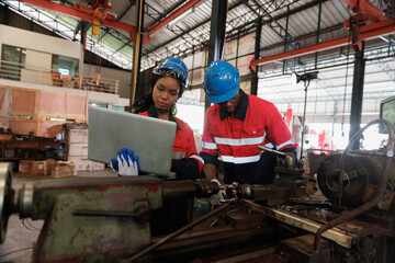 Fototapeta premium Two engineer heavy Industry Engineers Wearing Safety Uniform and Hard Hats Working on Laptop Computer. African American Technician and Female Worker Talking on a Meeting in a Factory.