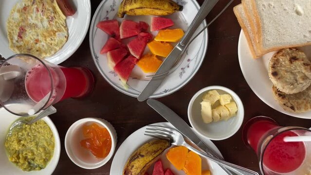 Tropical breakfast with fresh watermelon, papaya, banana, butter, white bread, English muffins, and watermelon juice on a wooden table