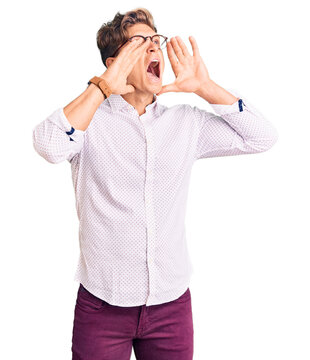 Young handsome man wearing business clothes and glasses shouting angry out loud with hands over mouth