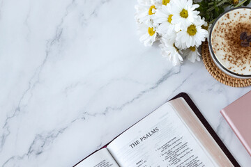 Psalms open holy bible book on white marble background with coffee cup and flowers. Top table view....