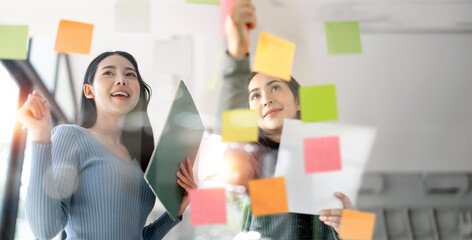 Two young creative woman planning on a glass board.