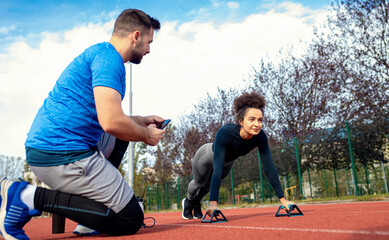 Young fitness couple exercising outdoors doung push ups on running track.