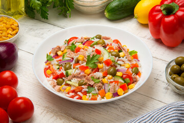 Tuna rice salad in a white porcelain salad bowl on a white rustic wooden table with ingredients. - 688676684