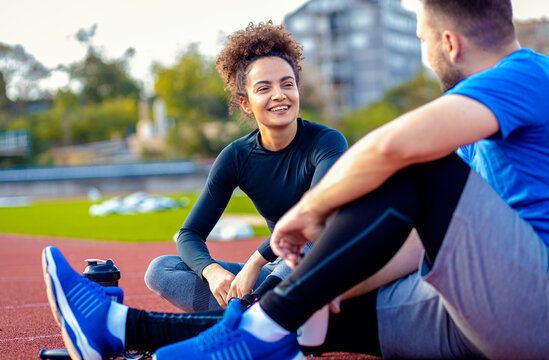 Young fitness couple resting after exercising outdoors, sitting on running track.