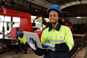 Portrait of female mechanical engineer worker in yellow hard hat and safety uniform using laptop standing at manufacturing area of industrial factory - obrazy, fototapety, plakaty