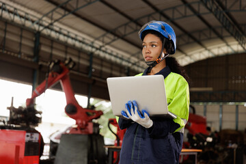Portrait of female mechanical engineer worker in yellow hard hat and safety uniform using laptop standing at manufacturing area of industrial factory