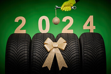 Winter car tires mechanic hand with wrench tool and christmas tree ball and text 2024 happy new year background