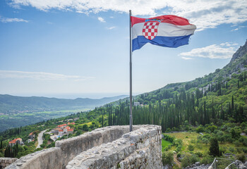 National flag of Croatia on a wall of Sokol fortress on background of green hills grown with...