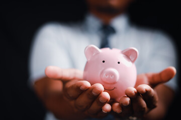 Financial concept, man holding piggy bank on wooden table Financial concepts, business, finance, investing, financial planning, investing for education