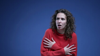 Scared young woman embracing herself hesitating showing fear and panicking on blue backdrop wearing...