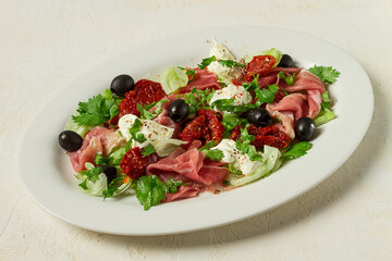 salad with dried tomatoes, prosciutto, soft cheese, olives, homemade, top view,