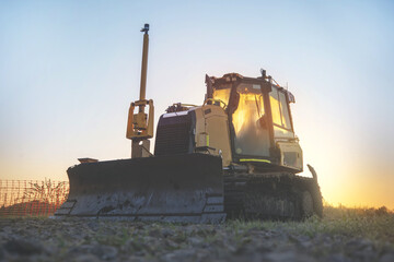 Silhouette of a bulldozer on a construction site in the early morning against the blue sky and the rising sun toned image