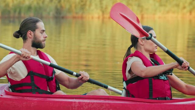 Good looking couple kayaking on pond or river during sunny day. People wearing vests. Rowing together with oars on kayak. Summer holiday. Having great vacation. Sport recreation. Tourism concept.