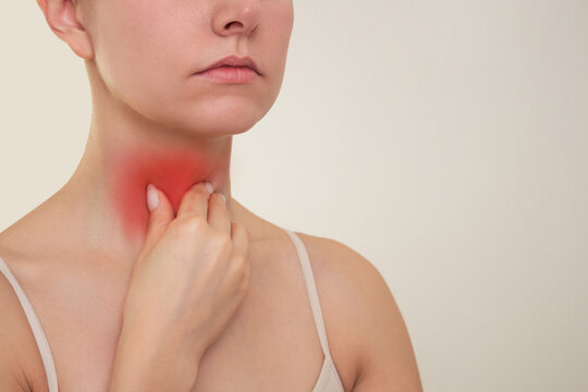 A young Caucasian brunette holds her hand on her red neck, suffers from sore throat, experiences pain when swallowing, loss of voice, thyroid disease. 