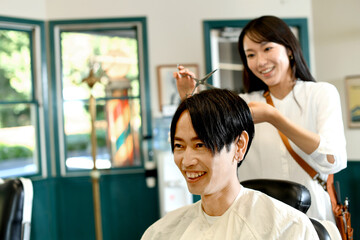 男性客の髪を切る美容師のアジア人女性