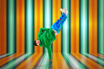 Young sportive man, dude wearing stylishly sport style cloth dancing breakdance elements, freezes against striped colorful background.