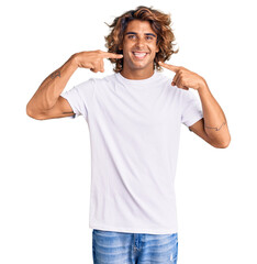 Young hispanic man wearing casual white tshirt smiling cheerful showing and pointing with fingers teeth and mouth. dental health concept.