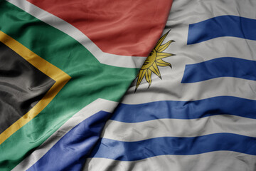 big waving national colorful flag of uruguay and national flag of south africa .