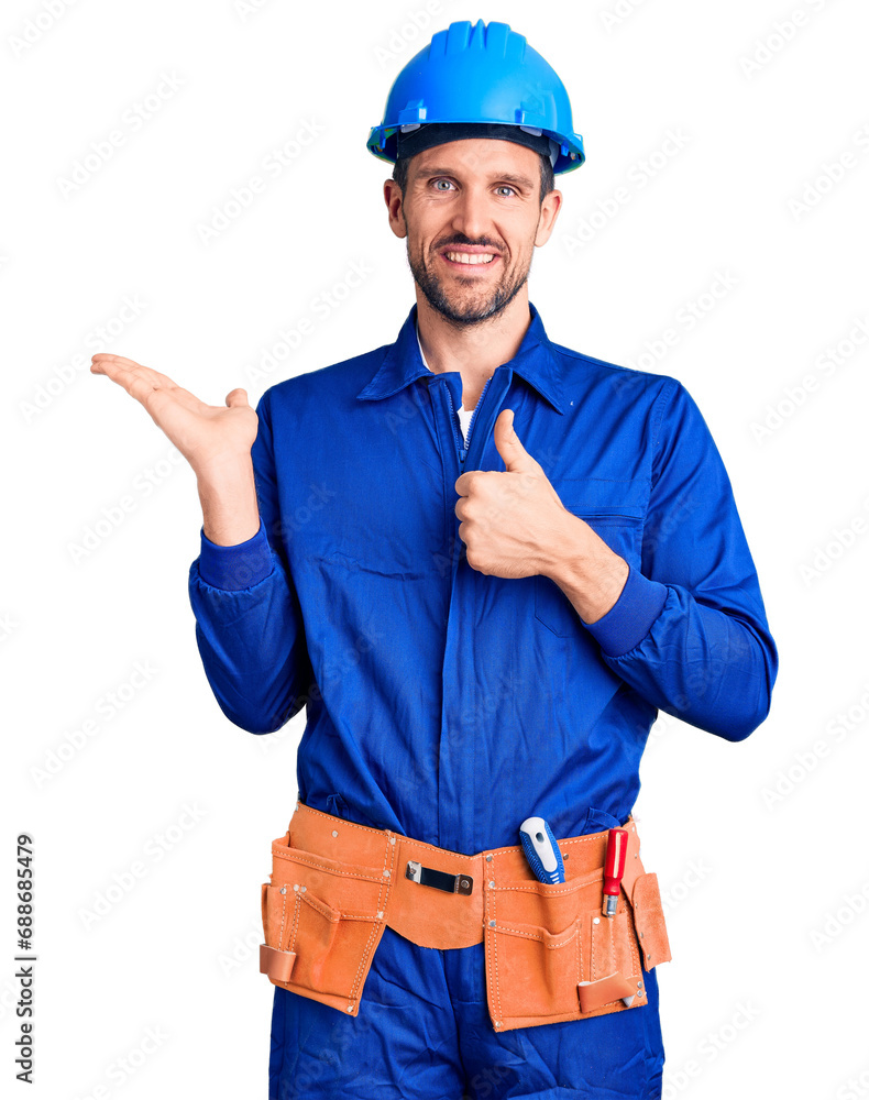 Canvas Prints young handsome man wearing worker uniform and hardhat showing palm hand and doing ok gesture with th