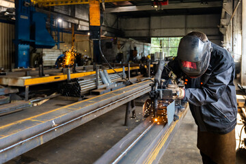 The welder works in the workshop. The moment of welding of metal structures. Beautiful sparks during welding of various metal elements in the workshop. The welder is working hard. - obrazy, fototapety, plakaty
