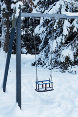 Children's playground in city park covered with snow. Empty swing, the children have already gone home, they will return in the spring.
