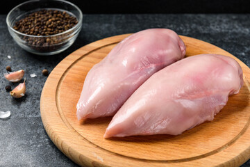 Raw chicken breast on wooden board on black background.