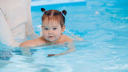 Fototapeta na wymiar Cute happy baby girl swimming with instructor in pool. Concept banner health care sport for kid