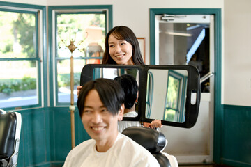男性客に鏡を見せる美容師のアジア人女性