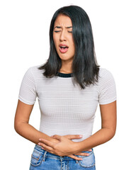 Beautiful asian young woman wearing casual white t shirt with hand on stomach because nausea,...