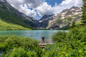 Mature Caucasian man, hiker standing on the edge of a lake in contrast to the water looking at a distant snow capped mountain pass, Gunsight Lake, Gunsight Pass, Glacier NP, Montana